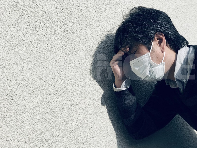 新型コロナウイルス？インフルエンザ？外出中に症状が悪化して壁にもたれかかるマスク姿の男性の無料写真